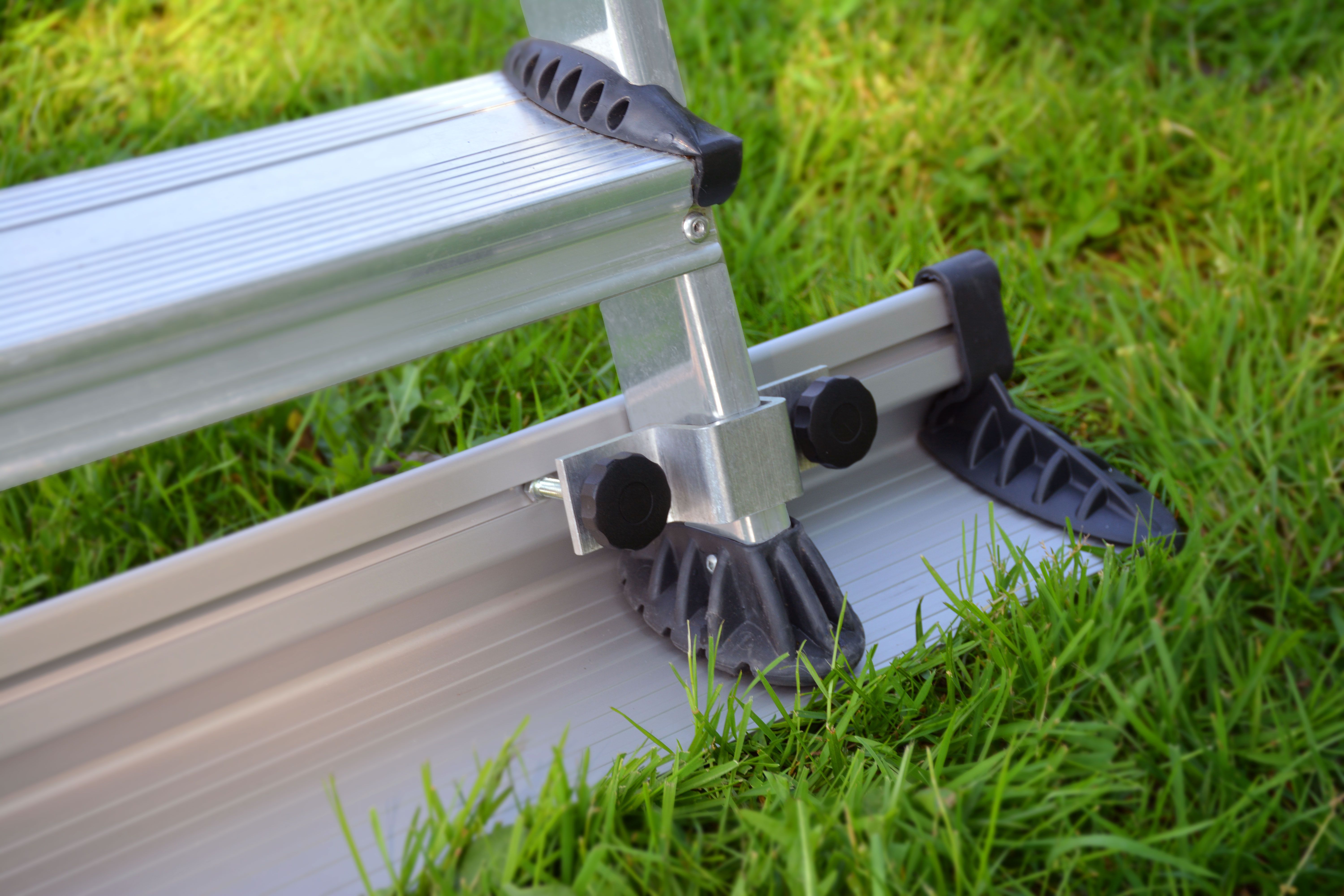 Aluminum ladder feet with black plastic grips resting securely on vibrant green grass.