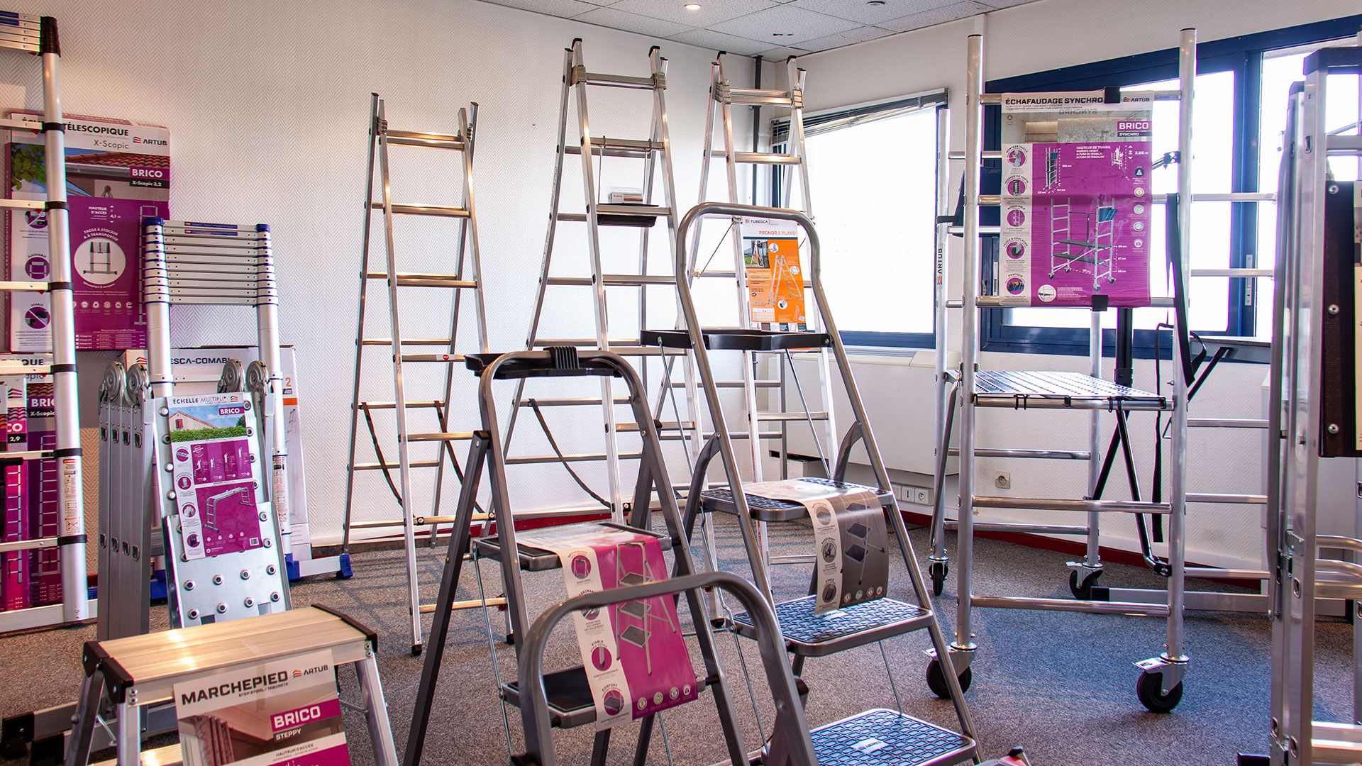 A collection of various silver ladders and step stools displayed in a bright store setting.