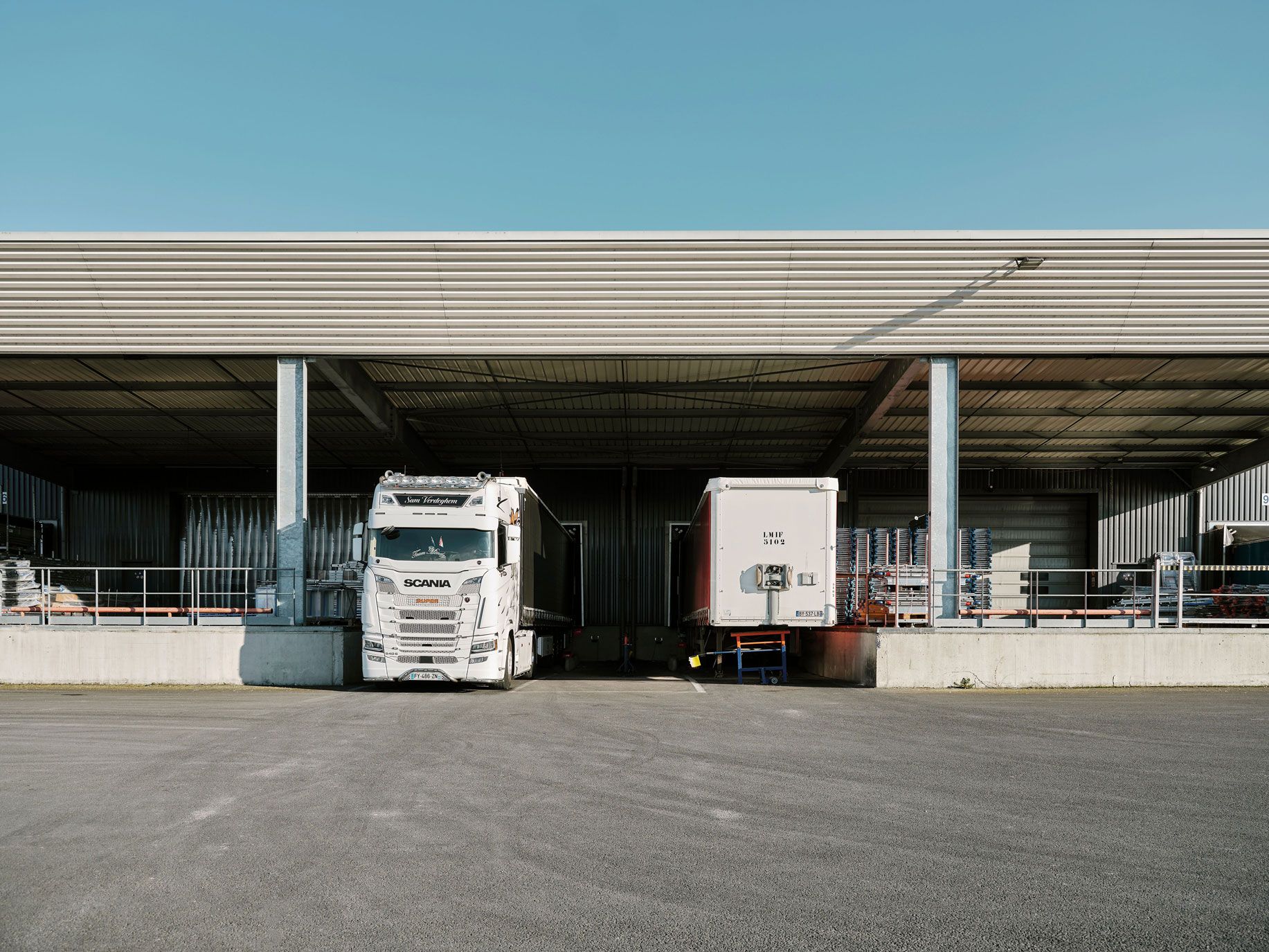 White semi-truck and trailer at a warehouse loading dock under clear sky.