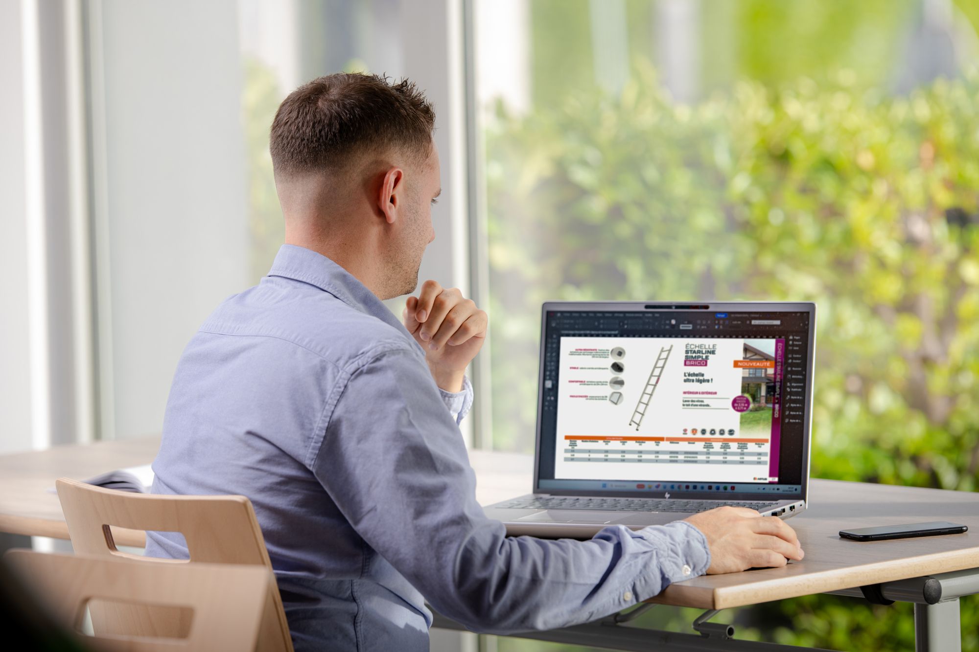 Man in blue shirt thoughtfully viewing a colorful presentation on his laptop at a desk.