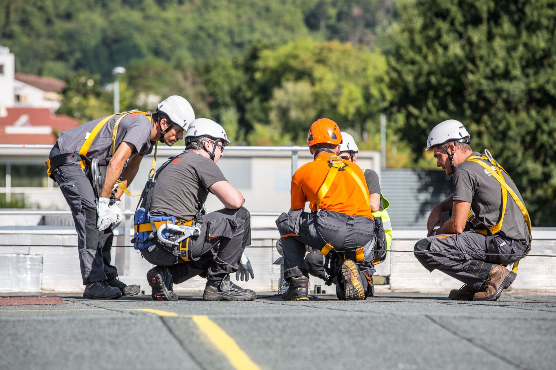Four construction workers in safety gear discuss a project on a rooftop.
