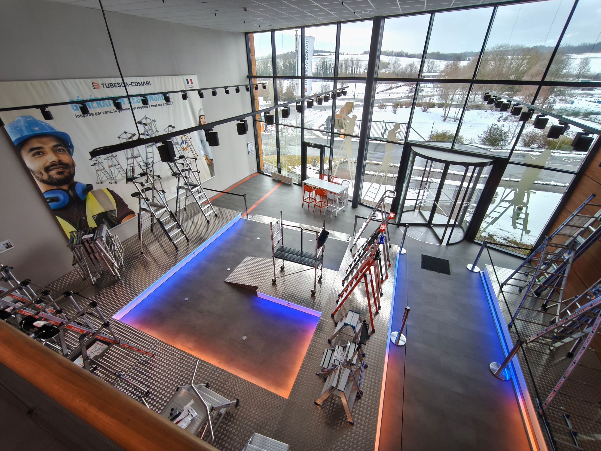 Modern showroom displaying various ladders and scaffolding with a large mural and glowing floor lines.