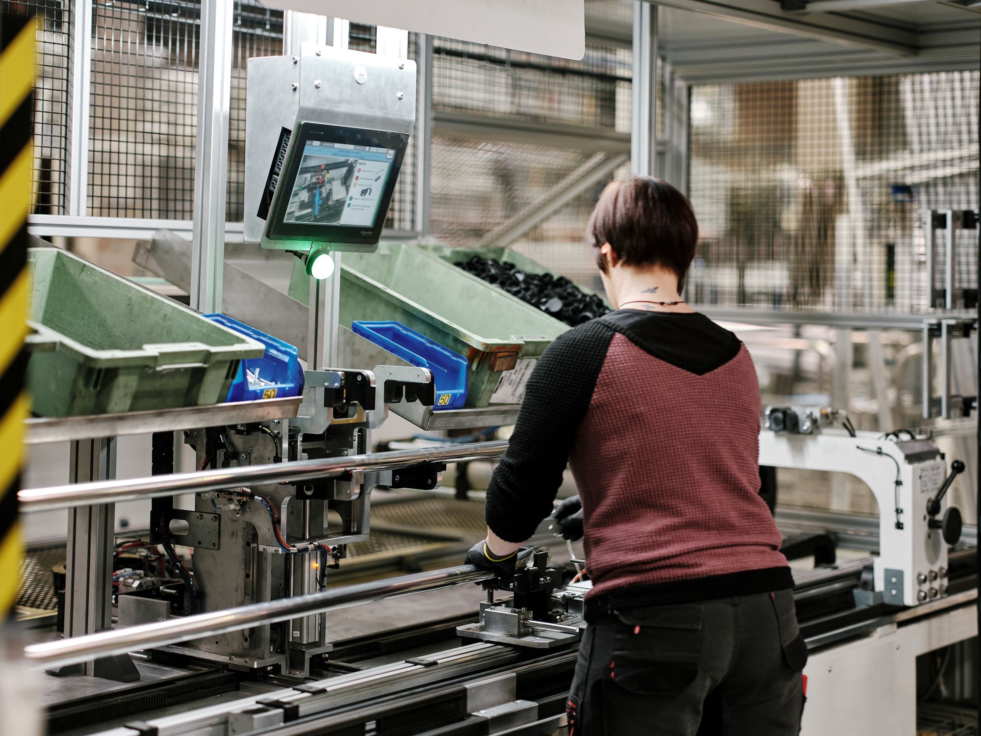 A worker assembles components on an automated production line with a digital display.
