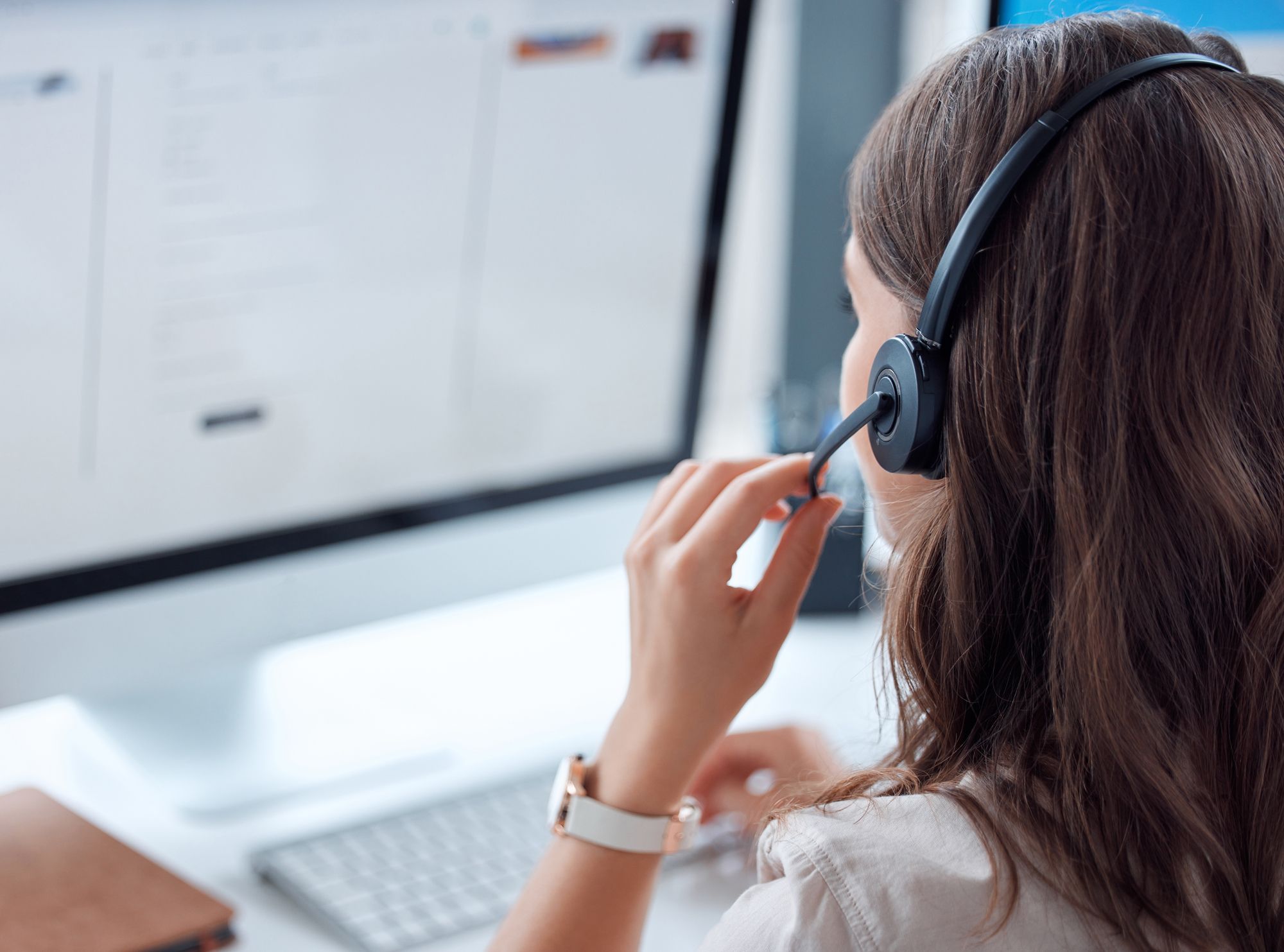Woman wearing a headset looks at a computer monitor, focusing on customer support.