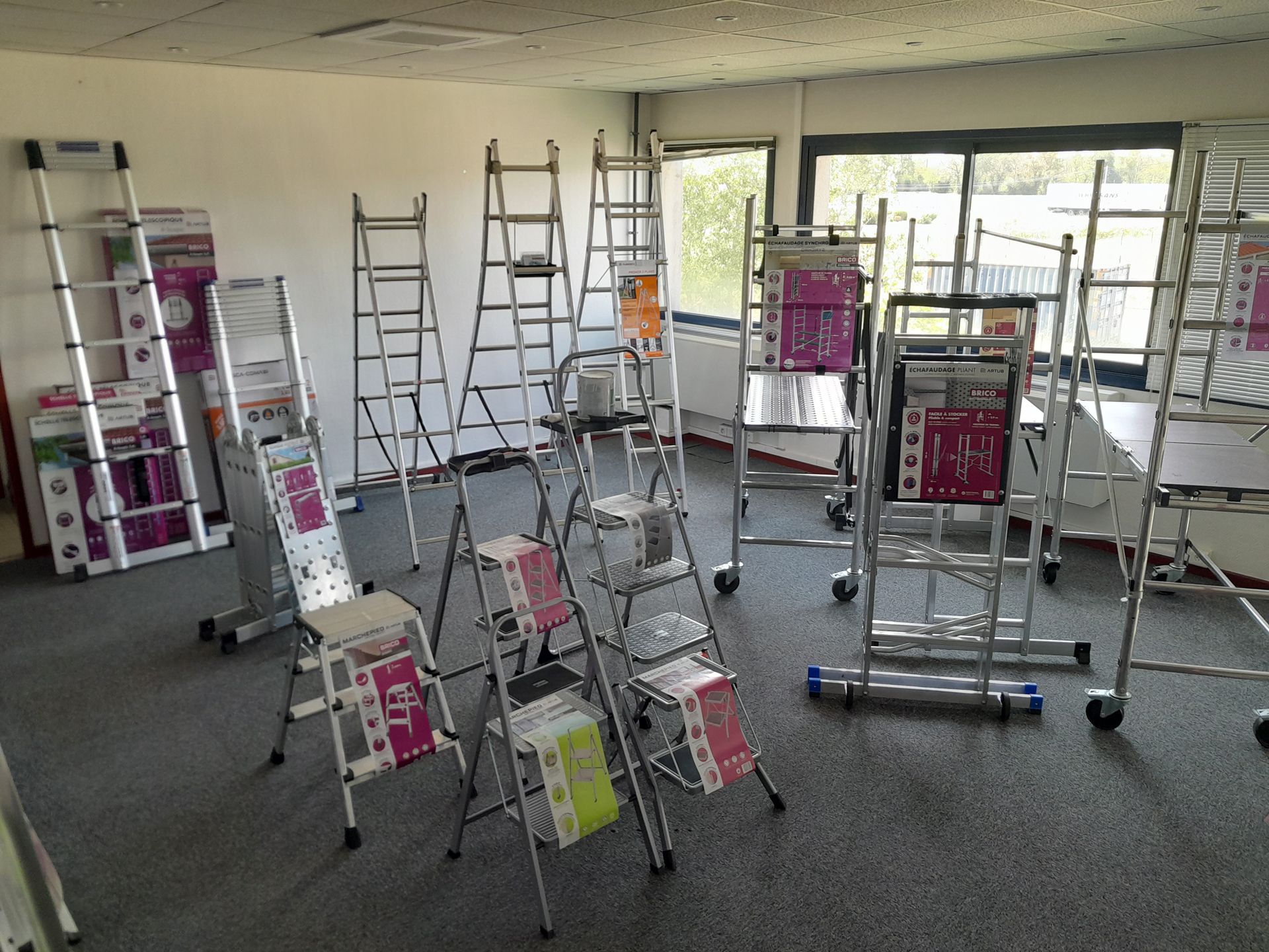 Various aluminum and steel ladders, including step stools, are displayed in a bright showroom.