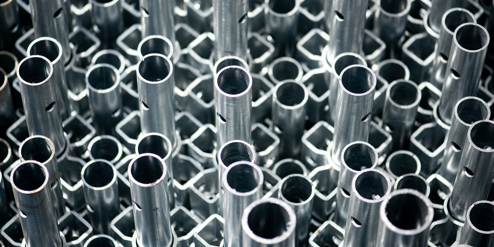 Tightly packed shiny metallic tubes and square rods, likely industrial components.