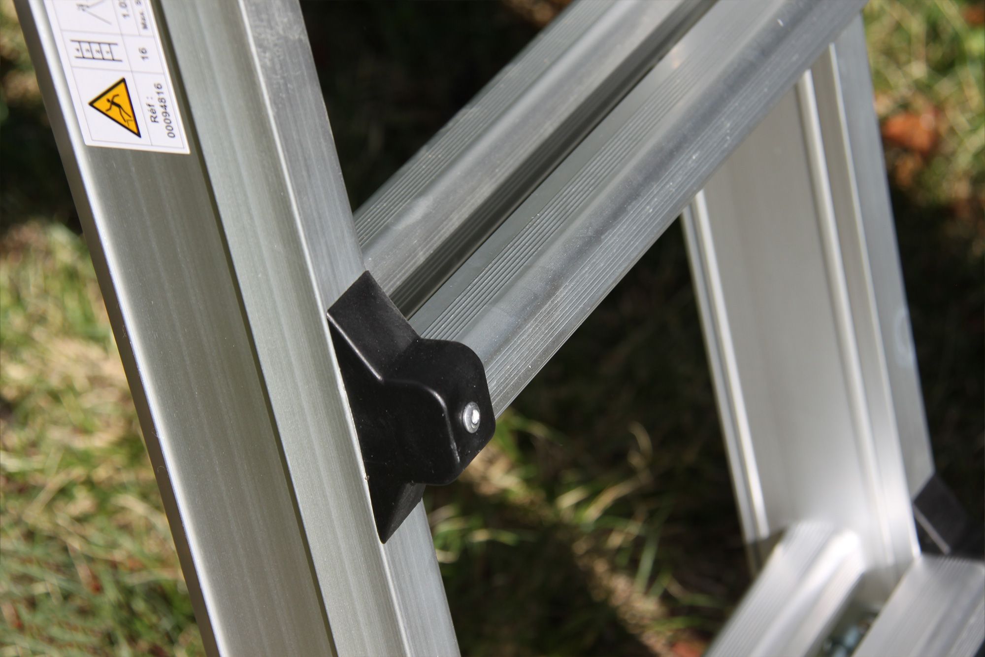 Close-up of a silver aluminum folding ladder with a yellow warning sticker.