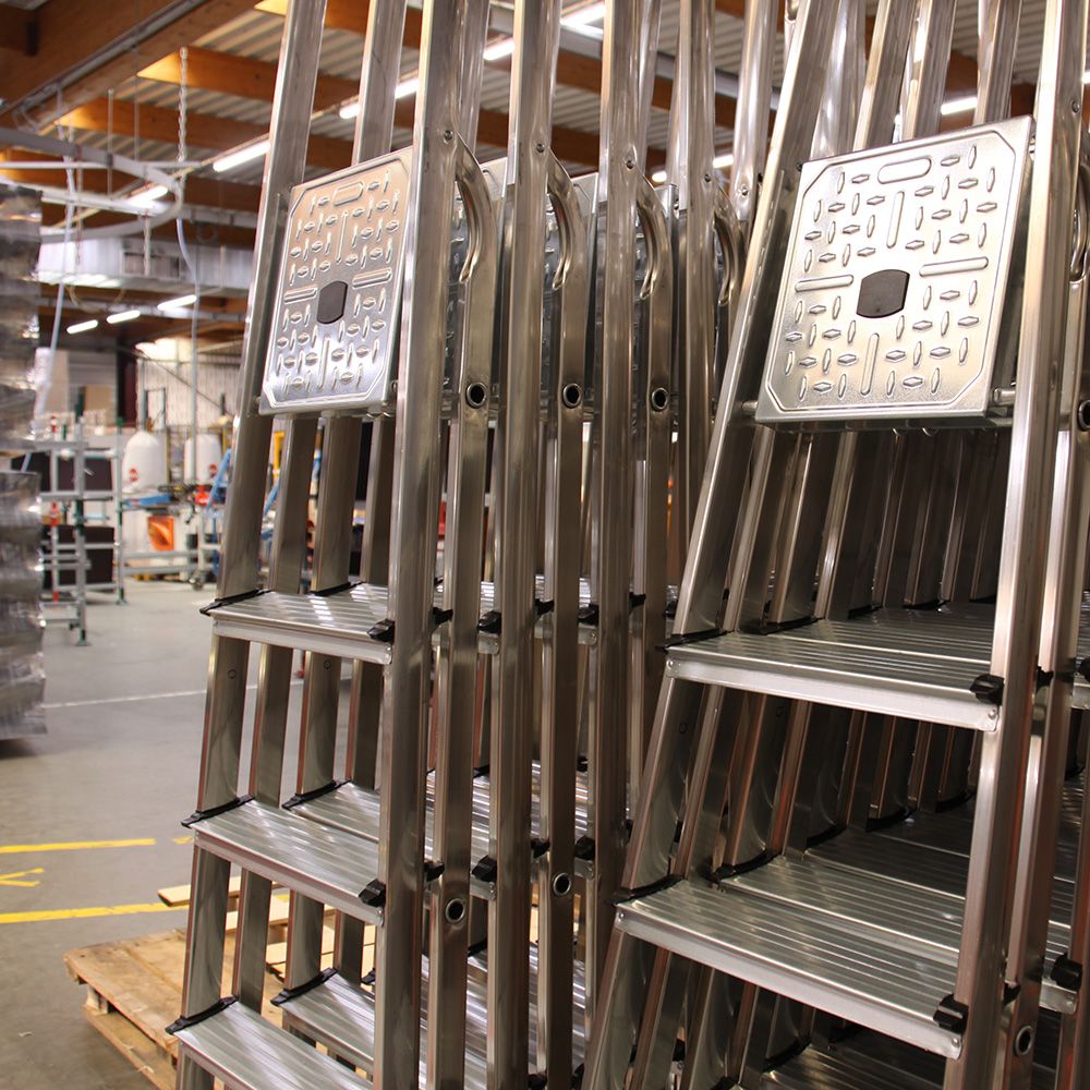 Stacked aluminum stepladders in a warehouse, featuring square labels on top platforms.