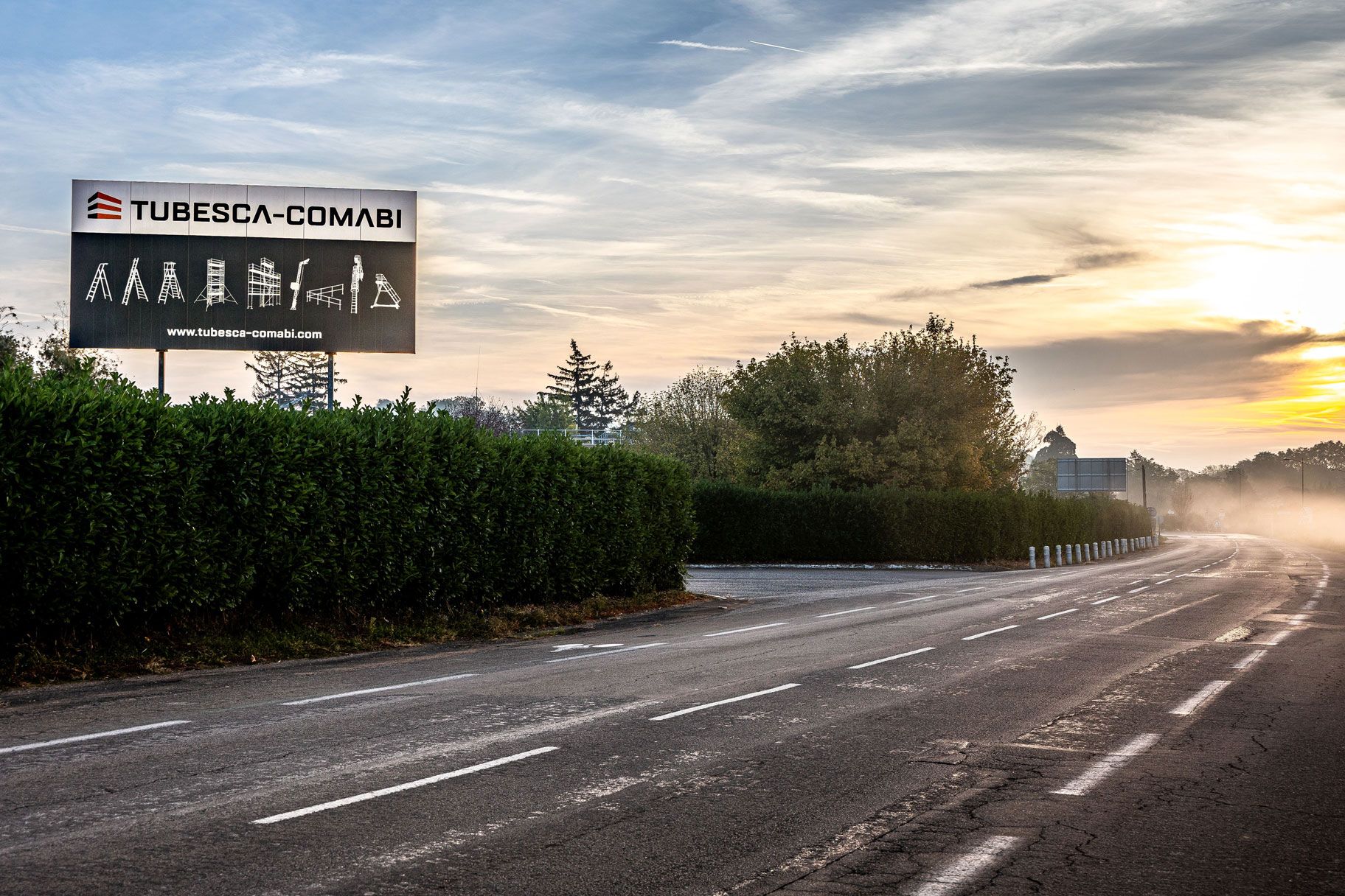 Tubesca-Comabi billboard with worker safety pictograms next to a road at sunset.